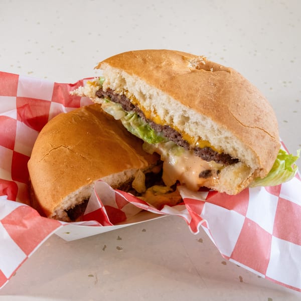 A cut-in-half burger with cheese, lettuce, and sauce in a red and white checkered paper.