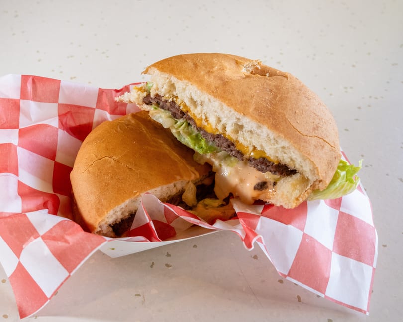 A cut-in-half burger with cheese, lettuce, and sauce in a red and white checkered paper.