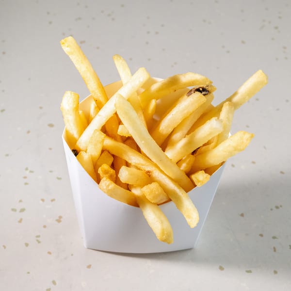 Golden french fries in a white paper container on a speckled white surface.