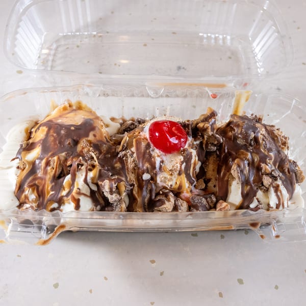 Banana split with vanilla ice cream, chocolate and caramel syrup, nuts, and a cherry in a plastic container.