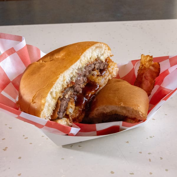 A cut-in-half burger with BBQ sauce and bacon in a red and white checkered paper tray.