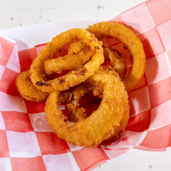 Golden-brown onion rings in a white paper tray lined with red and white checkered paper.