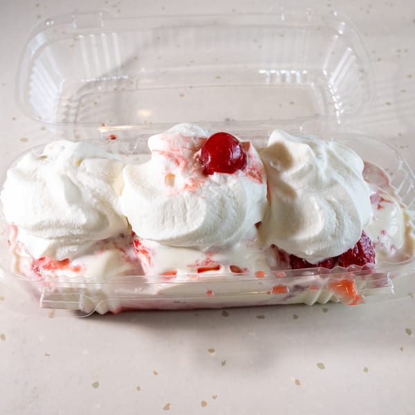 Strawberry shortcake with whipped cream and a cherry on top, in a clear plastic container.