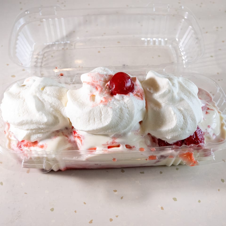 Strawberry shortcake with whipped cream and a cherry on top, in a clear plastic container.