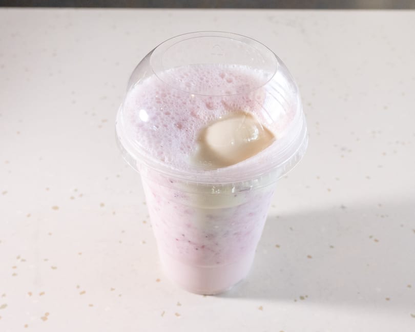 Pink berry smoothie with a scoop of vanilla ice cream and foam in a clear plastic cup.