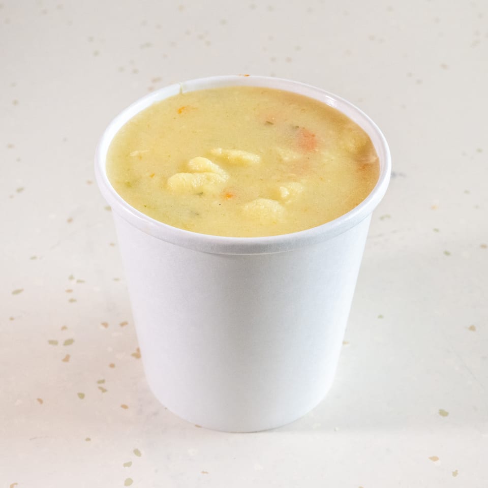 Creamy potato soup with visible chunks of potatoes and vegetables in a white cup.