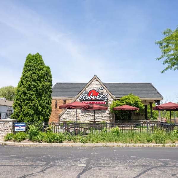 Robert's Frozen Custard restaurant exterior with stone facade, red umbrellas, and outdoor seating under a blue sky.