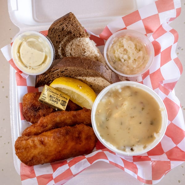 Fried fish, dark bread, lemon, butter, coleslaw, and tartar sauce in a takeout container.