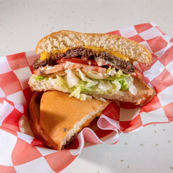 A cheeseburger cut in half, revealing a patty, melted cheese, tomatoes, lettuce, and sauce.