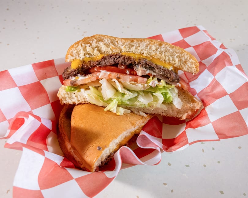 A cheeseburger cut in half, revealing a patty, melted cheese, tomatoes, lettuce, and sauce.