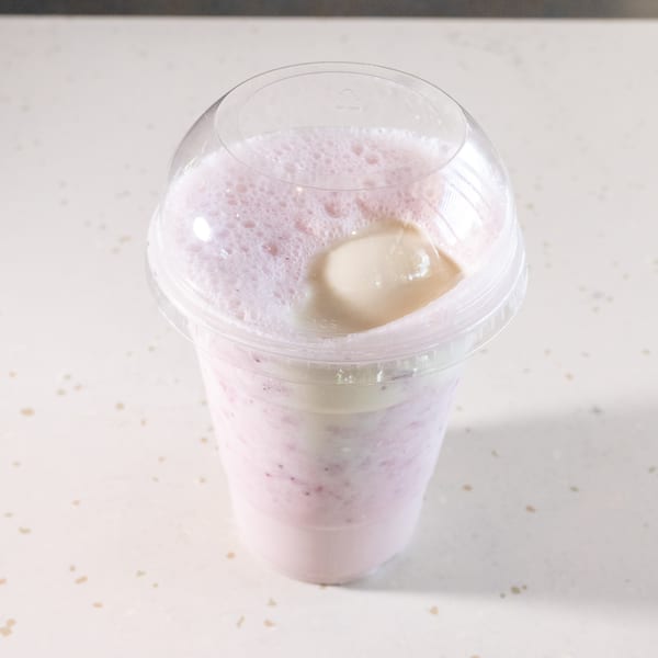 Pink berry smoothie with foam and a scoop of ice cream in a clear plastic cup.