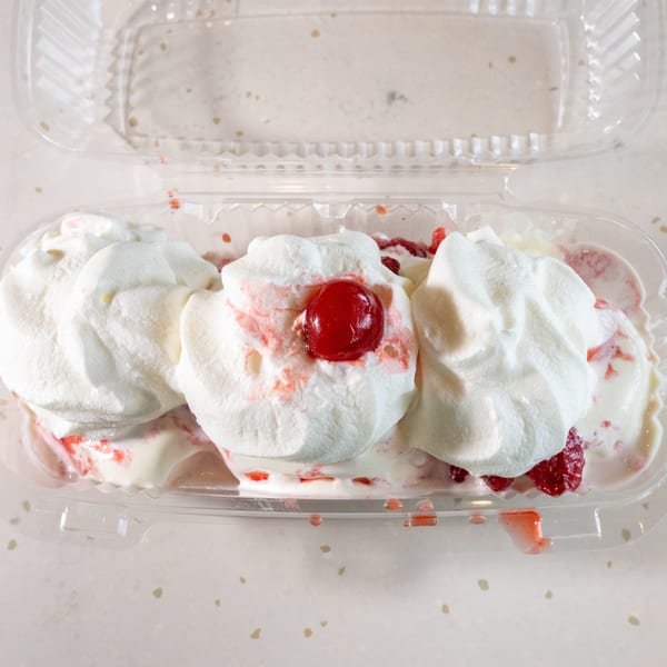 Strawberry shortcake dessert with whipped cream and a cherry in a clear plastic container.