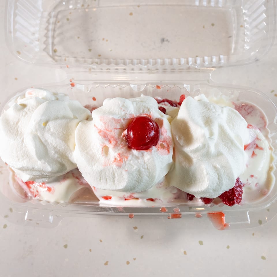 Strawberry shortcake dessert with whipped cream and a cherry in a clear plastic container.