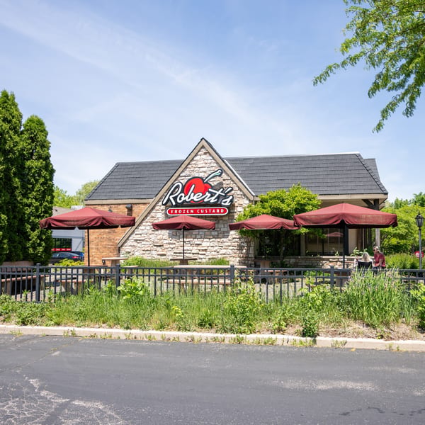 Robert's Frozen Custard restaurant with stone facade, red umbrellas, and outdoor seating on a sunny day.