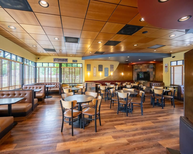 Spacious restaurant interior with booths, tables, chairs, and a fireplace, featuring warm lighting and wood accents.