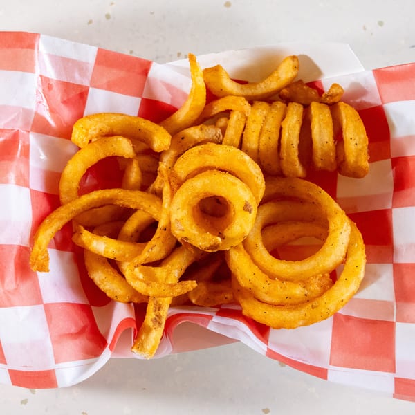 Golden curly fries seasoned with pepper, served in a red and white checkered paper container.